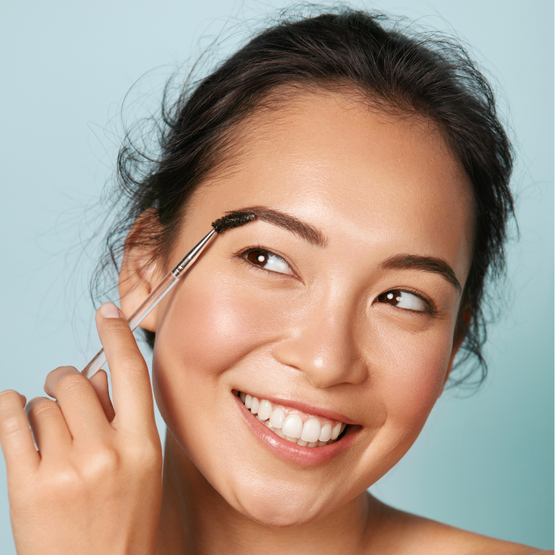 A happy woman brushing her perfect, full eyebrows into place after a professional eyebrow shaping and natural brow tint service