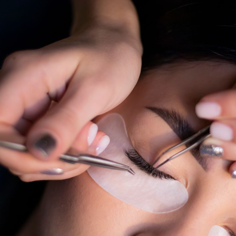 Close-up of a trained aesthetician performing a professional lash lift, using precision tweezers on a client's lashes at an aesthetic med spa.