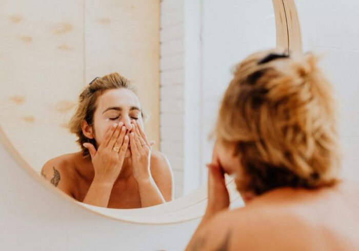 woman cleans face with her hands with tinted brows and lashes