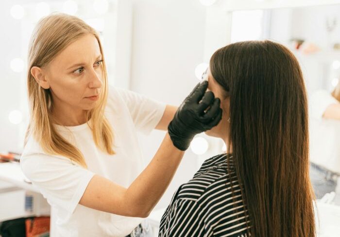 woman wearing latex gloves holds lash extensions to woman's face