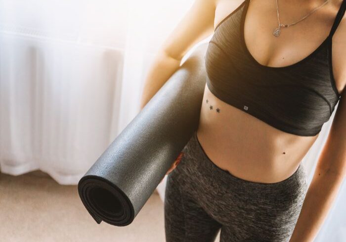 skinny woman in athetic clothing holding gym mat